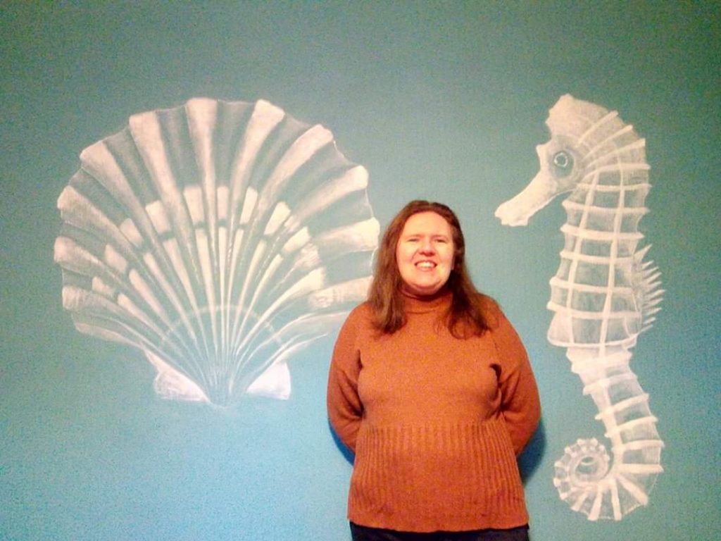 Helen in front of mural creation of seahorse and scallop shell